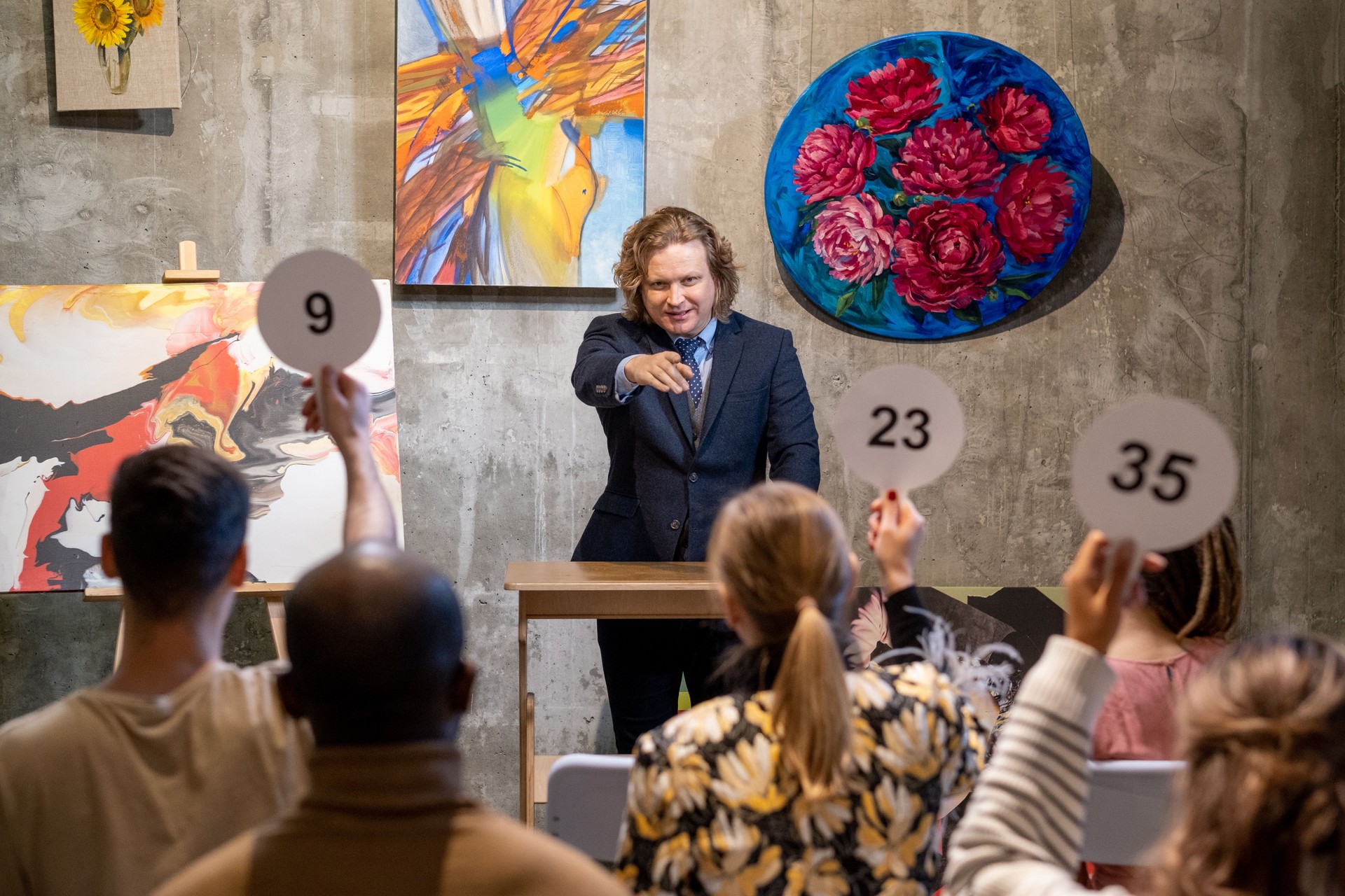 Male auctioneer pointing at one of people with auction paddles